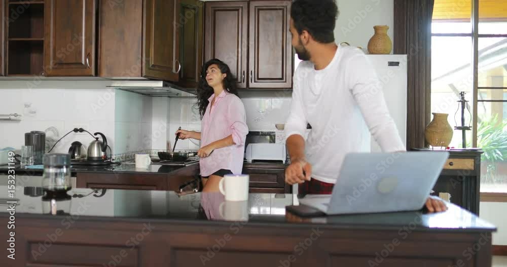 Couple In Kitchen, Man Using Laptop Computer While Woman Cooking Breakfast Talking Young Family Morning Communication Slow Motion 60 Couple In Kitchen, Man Using Laptop Computer While Woman Cooking Breakfast Talking Young Family Morning Communication Slow Motion 60