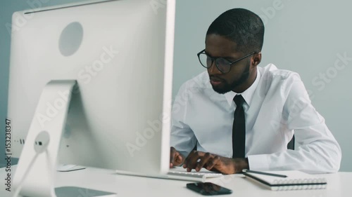 African young man working in office. When african office man sitting on desk with computer comming another worker and african man shaking his hand. photo