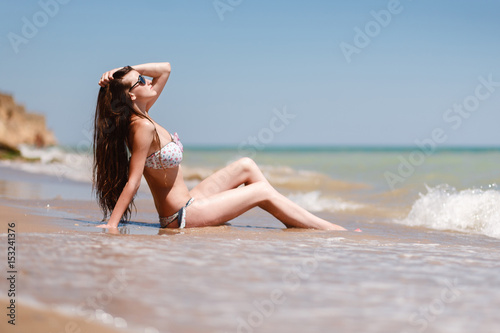 Wallpaper Mural Girl in a swimsuit and sunglasses, lying on stomach on a large stone against the sea, the mountains and the beach. Summer holidays, vacation and beach concept. Enjoy the warmth of the sun. Torontodigital.ca