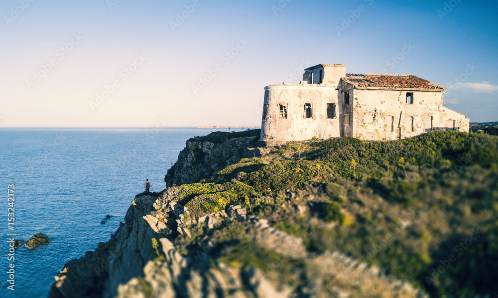 A man standing on a high cliff enjoying the view of an Italian coast with the Mediterranean sea Below him. Porto Cervo - Emerald Coast, Sardinia - Italy
