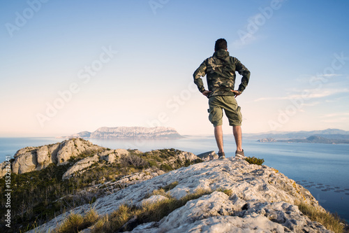 A traveler on the top of the mountain is enjoying the stunning view at sunset in Sardinia, Italy.