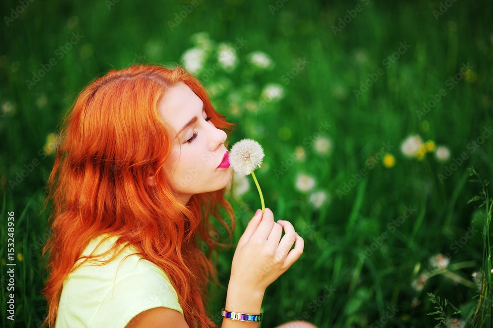Beautiful young woman with closed eyes smelling a flower on a blurred background of green grass in summer Park. Close-up