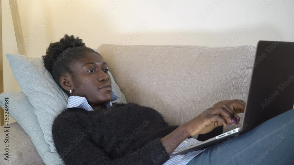 Portrait afro american girl using laptop at home. Lady lies on the couch chatting online or surfing internet or study. Beautiful model in flat enjoy free time. Portrait afro american girl using laptop at home. Lady lies on the couch chatting online or surfing internet or study. Beautiful model in flat enjoy free time.