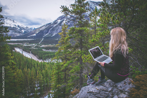 Girl with a laptop working on the top of the mountain