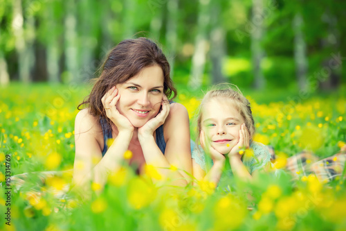 Mother and daughter lying on green summer meadow with blooming yellow flowers