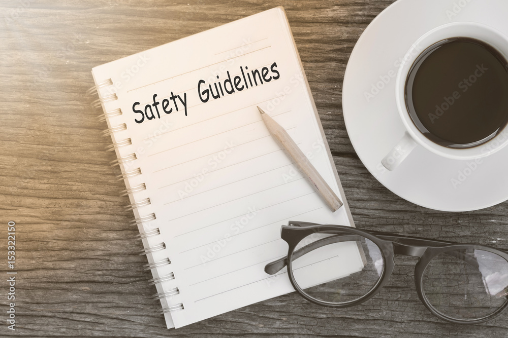 Plakat Safety Guidelines text written on a notebook with glasses, pencil and coffee cup on wooden table.