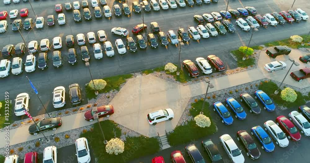 Dealership car lot, many beautiful new vehicles for sale, many brands, aerial view.

