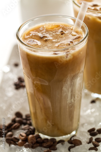 Tasty cold refreshing drink with coffee, milk and ice in glass on ice background. Closeup.