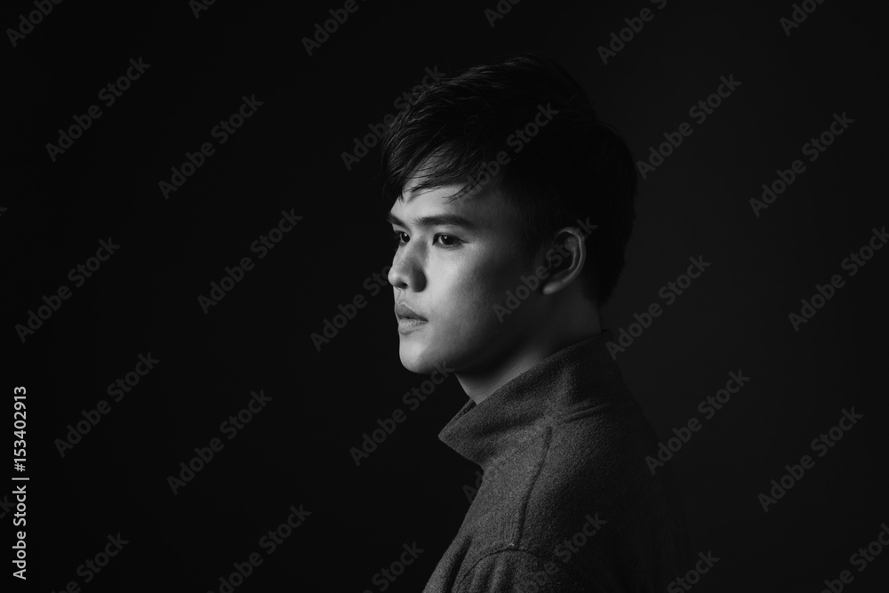 Attractive asian man looking down to his side on dark studio background. Attractive asian man looking down to his side on dark studio background.