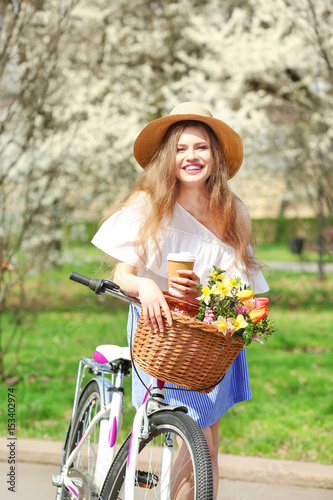 Beautiful smiling girl near bicycle with cup of coffee in park