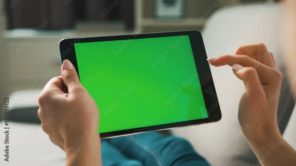 Woman hands using black tablet with green screen, lieng on sofa at home. View from the back. Chroma key. Close up.