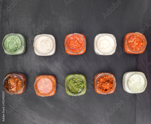selection of delicious sauces inside jars over slate