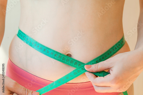 Close up of female hands measuring waist with measuring tape, dieting concept. Fat woman.