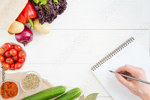 Close-up partial view of person holding pencil and writing recipe in cookbook while cooking