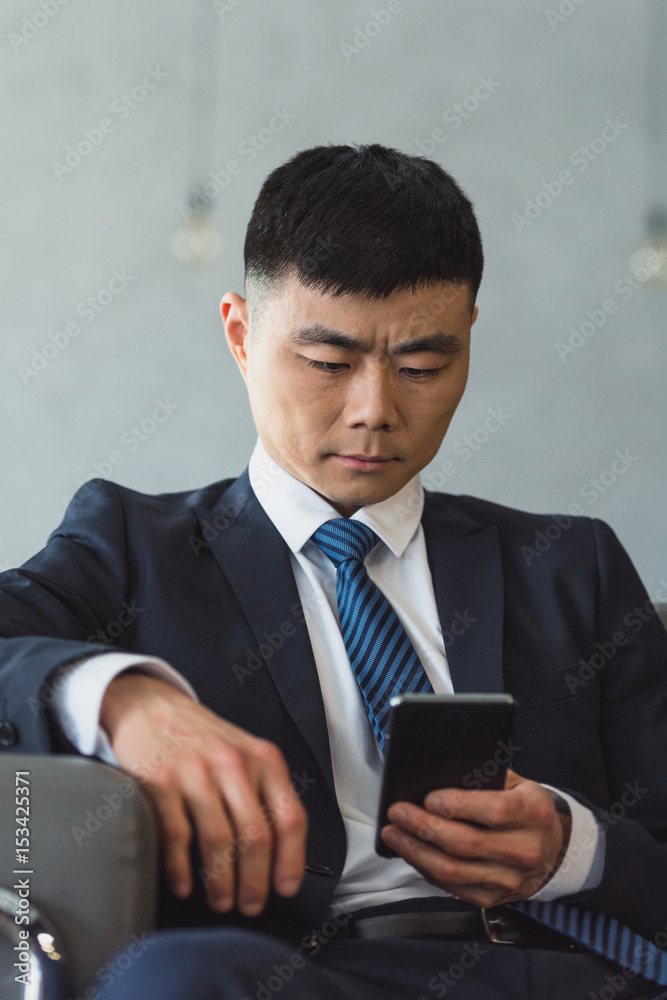 asian businessman sitting on sofa using smartphone in office asian businessman sitting on sofa using smartphone in office