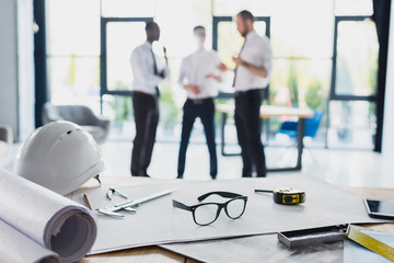 various architecture supplies on workplace with architects behind, focus on foreground