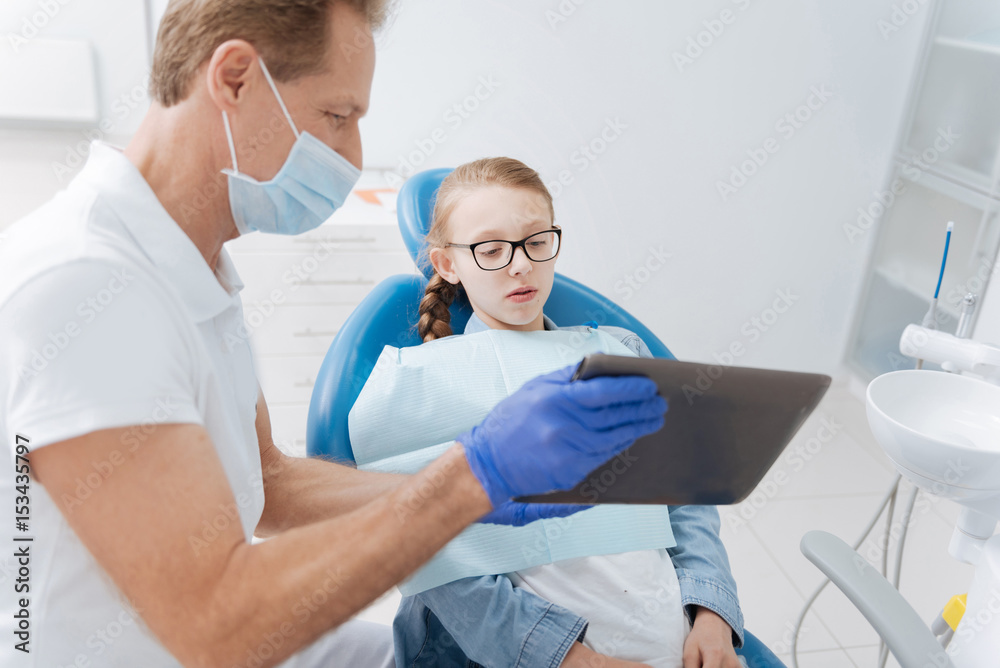 Fototapeta premium Bright attentive dentist showing updates on patients progress