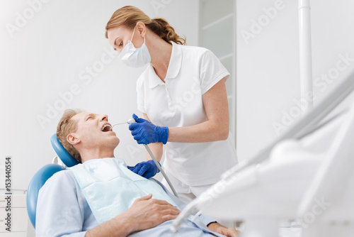 Pleasant mature gentleman having his teeth treated by professional