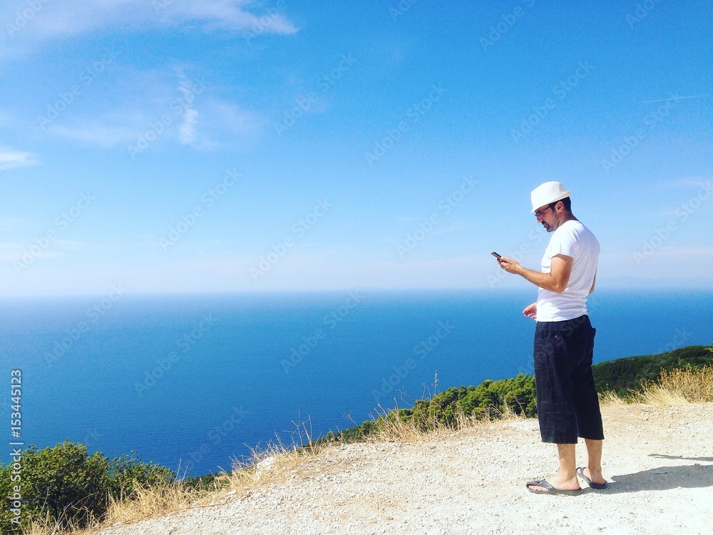 Man checking phone, standing on the cliff, looking at smartphone