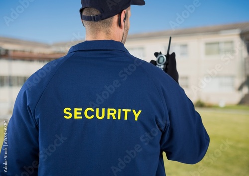 Rear view of security guard using radio against house
