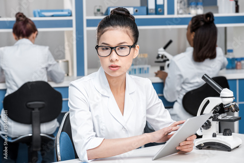 asian scientist in lab coat with microscope and digital tablet working in chemical lab  scientists group behind
