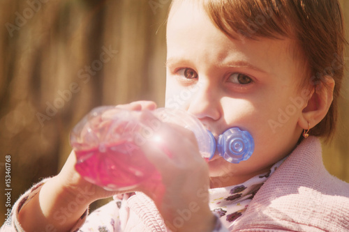 Little beautiful girl child drinking tasty natural juice outdoors. (Vitamins, health, thirst, happy childhood concept)
