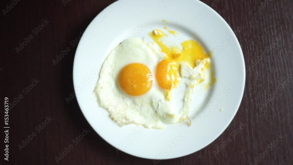 Top view of woman hands cutting piece of fried egg with knife and fork. Close up of eating fried eggs. Traditional morning breakfast eggs in white plate. Eating eggs fried Top view of woman hands cutting piece of fried egg with knife and fork. Close up of eating fried eggs. Traditional morning breakfast eggs in white plate. Eating eggs fried