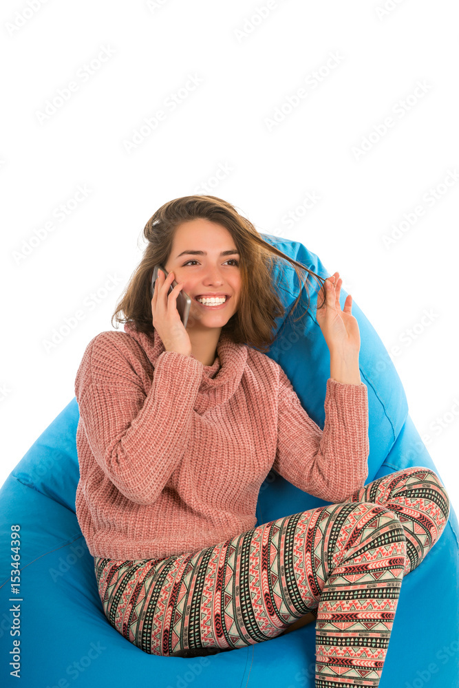 Laughing cute woman sitting on blue beanbag chair and talking on the phone isolated on white background Laughing cute woman sitting on blue beanbag chair and talking on the phone isolated on white background