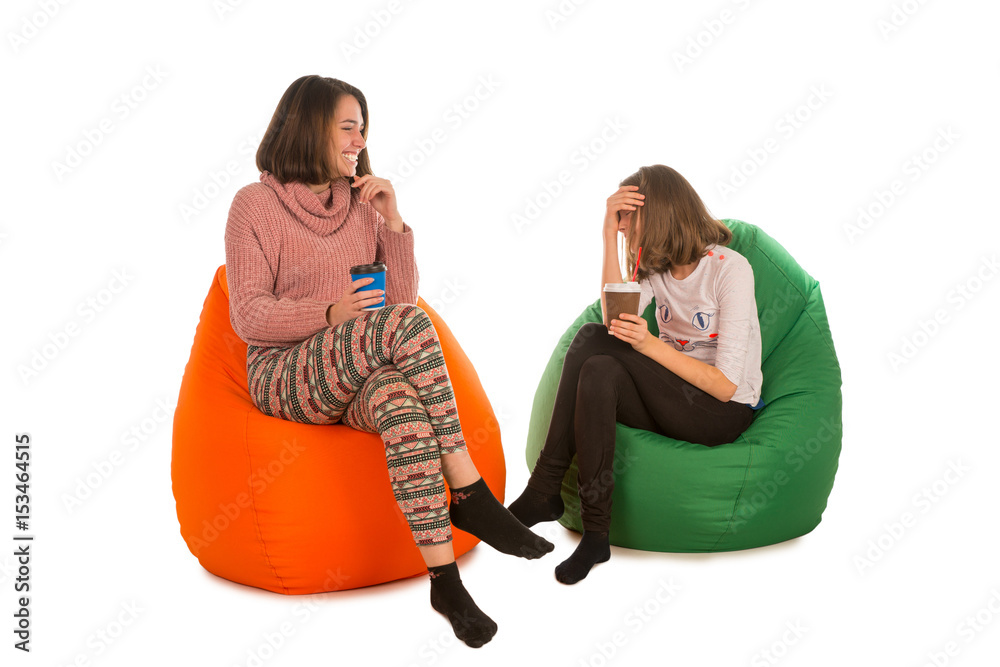 Young woman and laughing girl sitting on beanbag chairs and drinking coffee