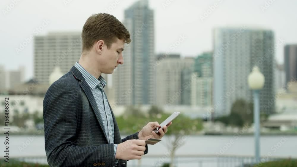 Young attractive guy is buying something over the Internet on a street of Coronado