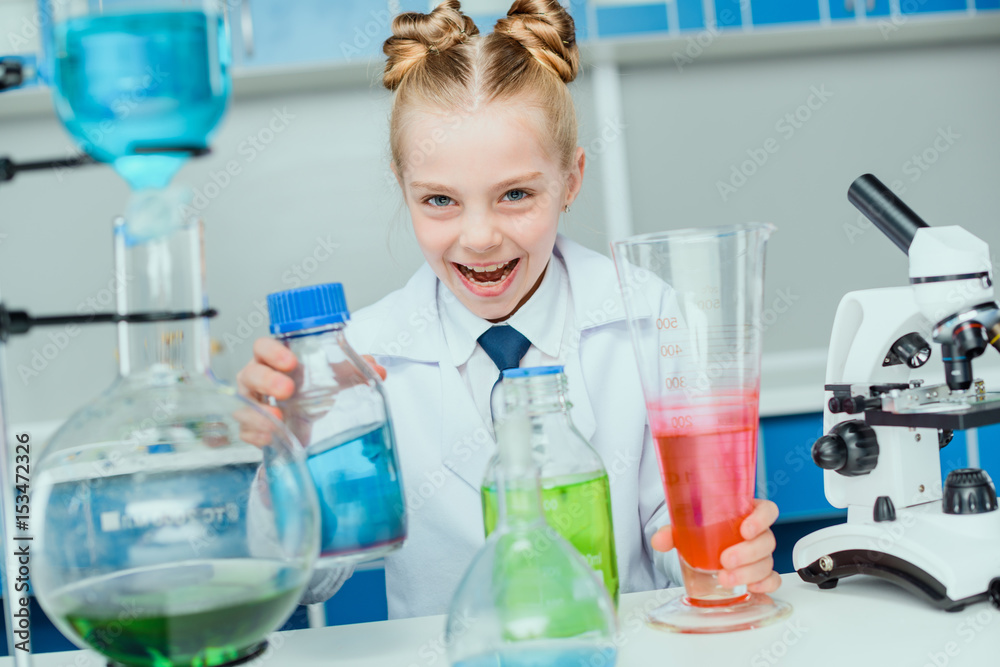 Schoolgirl in white coat making experiment with reagents in science laboratory Schoolgirl in white coat making experiment with reagents in science laboratory
