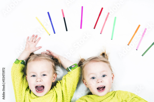 Two identical beautiful twins girls having fun on a white background with multi-colored markers in bright green clothes photo