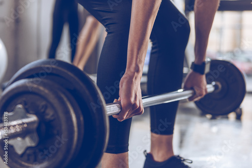 Cuadro en lienzo Close-up partial view of sportswoman lifting barbell at gym workout