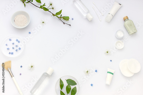 White cosmetics flat lay frame with flowers and leaves. Clean beauty concept