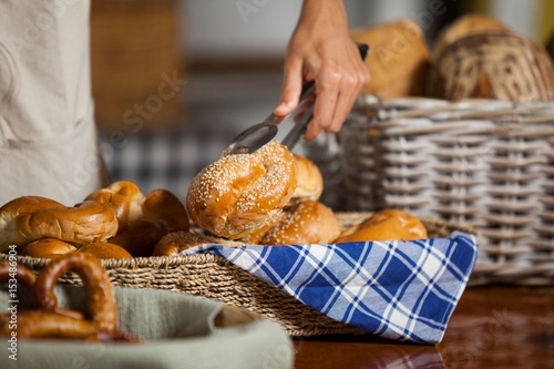 Staff holding bread with tong in bakery shop