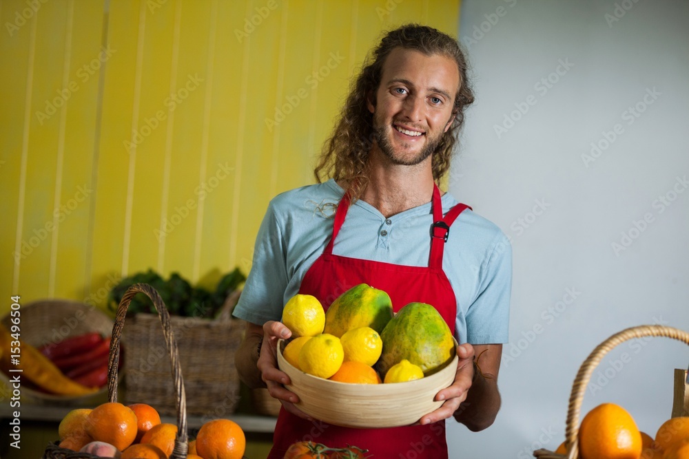 Smiling male staff holding fruits in basket at organic section Smiling male staff holding fruits in basket at organic section