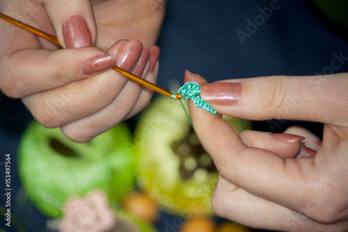 Woman knitting a crocheted flower from blue threads against a background of multicolored tangles