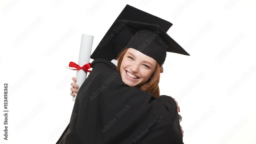 Two happy Caucasian boy and girl in black robes and square academical caps hugging each other on white background and smiling laughing in slowmotion Two happy Caucasian boy and girl in black robes and square academical caps hugging each other on white background and smiling laughing in slowmotion