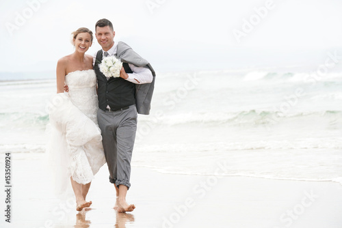 Happy bride and groom walking barefoot on the beach by the sea © goodluz