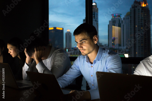 business team working late at night with lights off and computers laptop screen light on. Business people working hard concept. 20-30 year old. photo