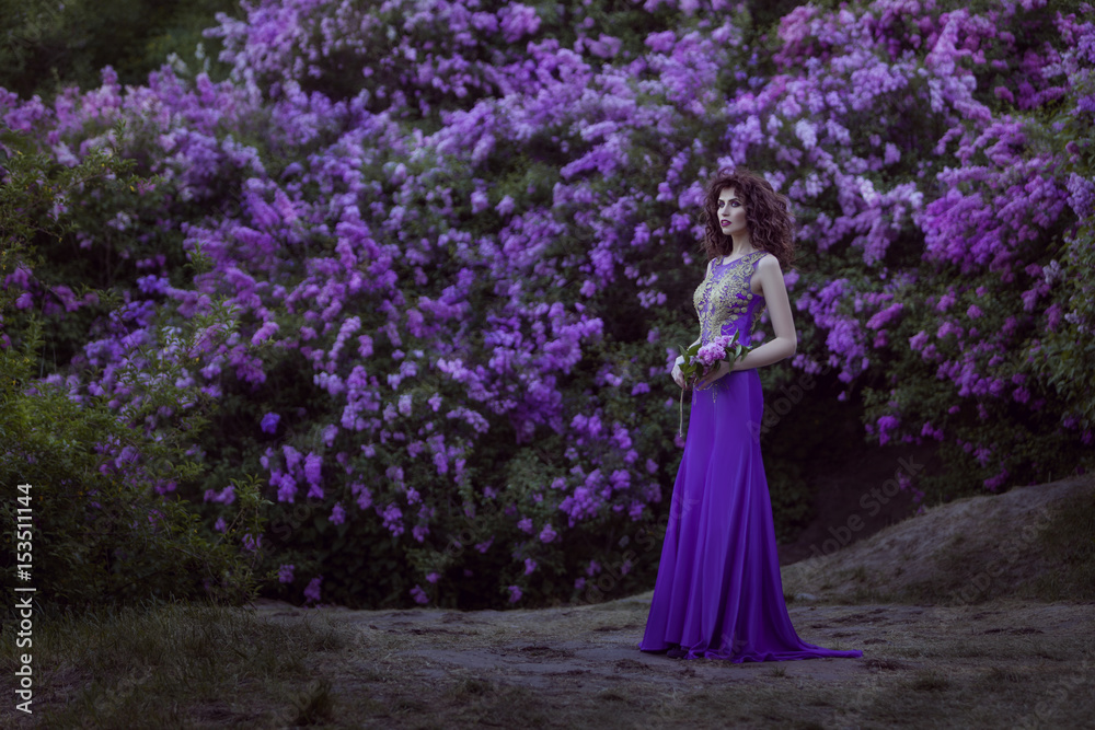 Woman against the background of blossoming lilac flowers, she is dressed in a lilac dress.