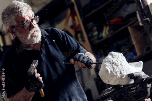 Fotografia Senior sculptor working on his marble sculpture in his workshop with hammer and chisel
