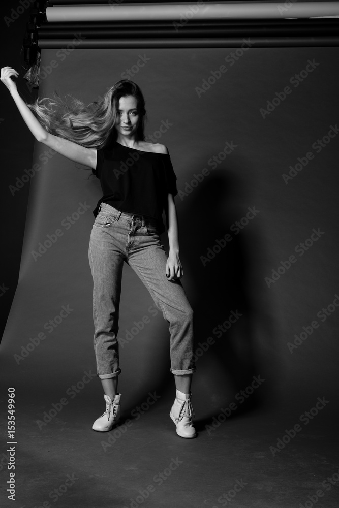 Black and white portrait of blonde girl in t-shirt and jeans on dark background throws the hair model tests. Black and white portrait of blonde girl in t-shirt and jeans on dark background throws the hair model tests.