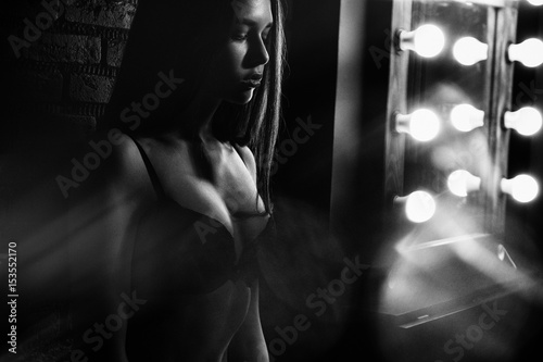 Black-and-white photo of a young girl standing amid the lamps in black lingerie.