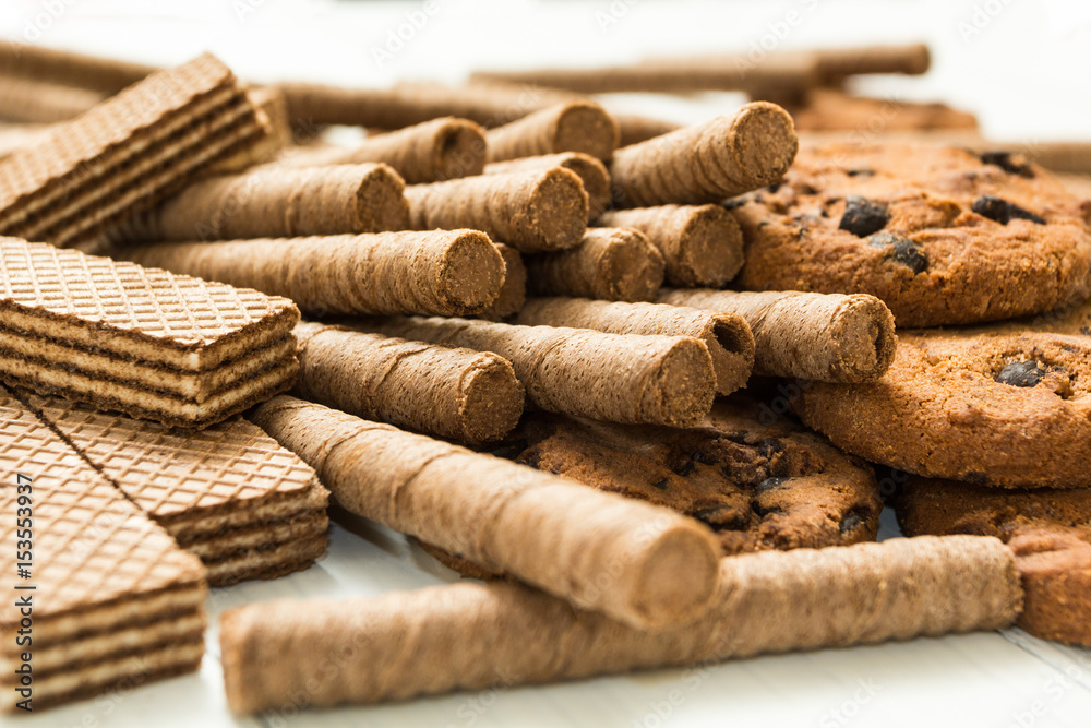 Chocolate waffle rolls, biscuits and classic waffle on a wooden white table. Fresh sweets. Chocolate waffle rolls, biscuits and classic waffle on a wooden white table. Fresh sweets.