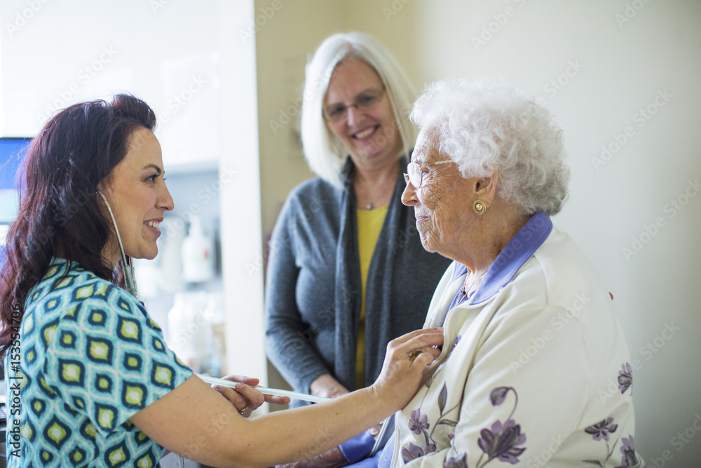 Daughter looking at female doctor examining mother in hospital ward Daughter looking at female doctor examining mother in hospital ward