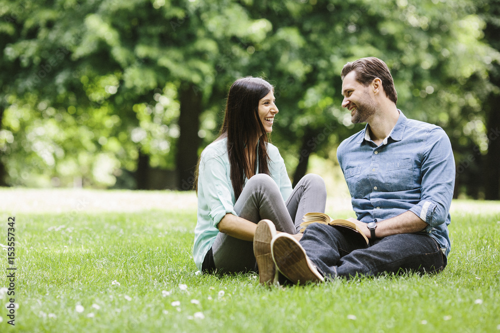 Happy couple looking at each other while relaxing on grassy field in park Happy couple looking at each other while relaxing on grassy field in park