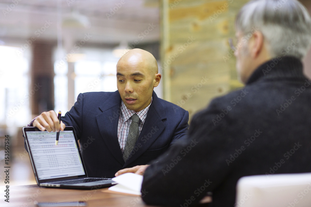 Businessman explaining to colleague over laptop in office meeting Businessman explaining to colleague over laptop in office meeting