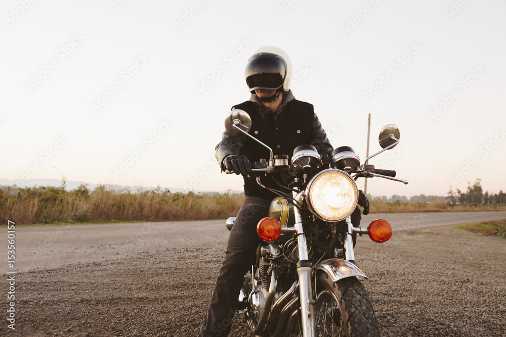 Male biker sitting on motorcycle by road against clear sky during sunset Male biker sitting on motorcycle by road against clear sky during sunset