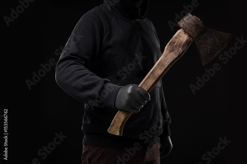 A man in gloves holds an ax in his hands against a black background